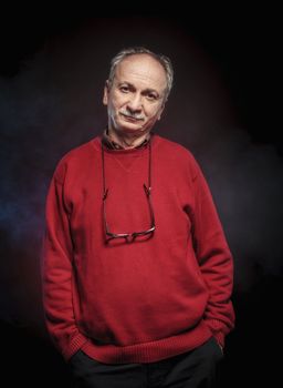 Portrait of an elderly man wearing red jacket on a dark background