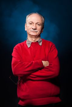 Portrait of a successful elderly man in a red sweater on a dark blue background