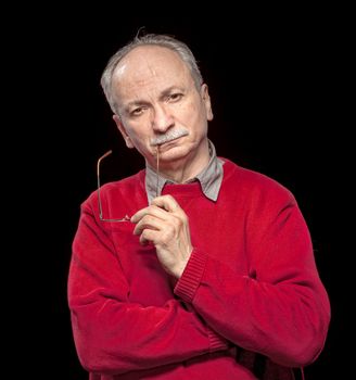 Portrait of an thoughtful  elderly man with glasses in his hands on a dark  background