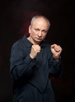 Mature man in boxer pose with raised fists on black background
