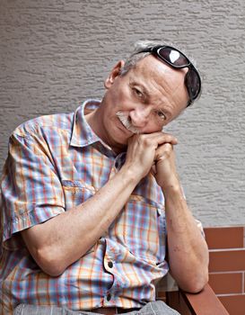 Portrait of an thoughtful elderly man with scratched hands and sunglasses on his forehead