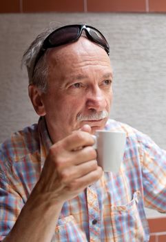 Portrait of smart old man drinking cup of coffee while sitting outside