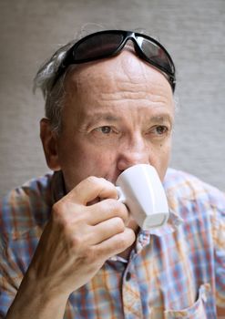 Portrait of smart old man drinking cup of coffee while sitting outside