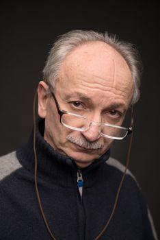 An elderly man with glasses looks skeptically on a dark background