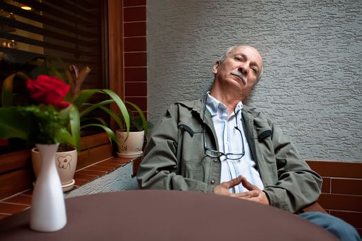 An elderly man sitting relaxed in a cafe waiting for a cup of coffee