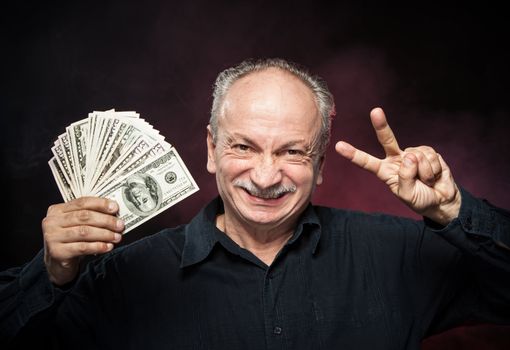 Lucky old man holding with pleasure group of dollar bills. Focus on face