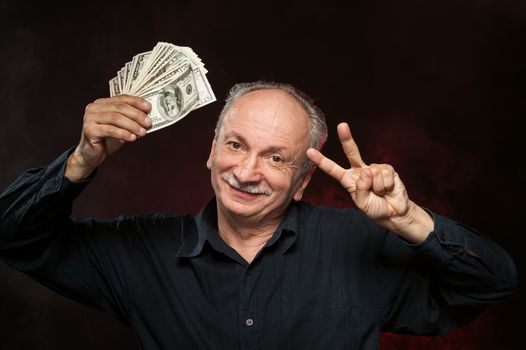 Lucky old man holding group of dollar bills and fingers in victory sign