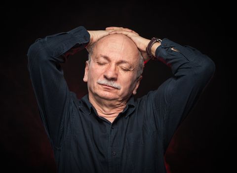 Portrait of an elderly man with hands behind head and closed eyes