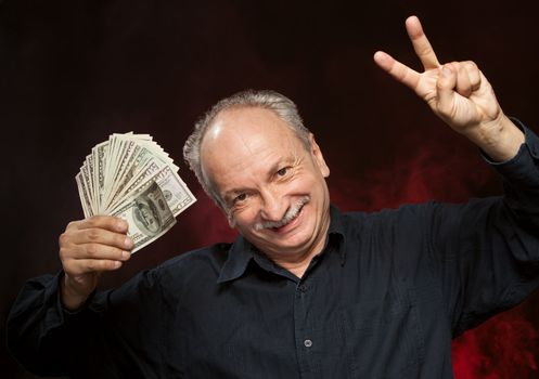 Lucky old man holding group of dollar bills and fingers in victory sign