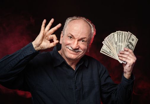 Lucky old man holding with pleasure group of dollar bills