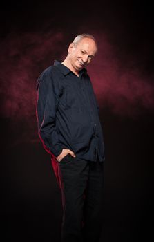 elderly man in a black shirt standing on a dark background