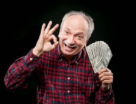 Happy elderly man showing fan of money and sign OK with fingers