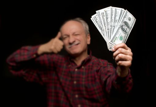 Happy elderly man showing fan of money and sign OK with fingers. Focus on money