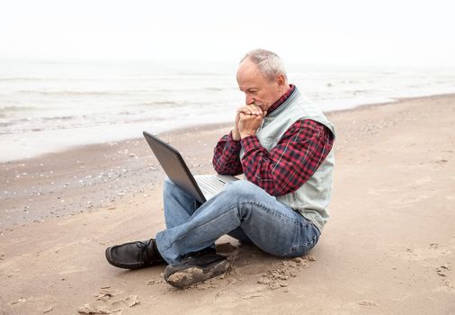 Old man sitting with notebook on beach