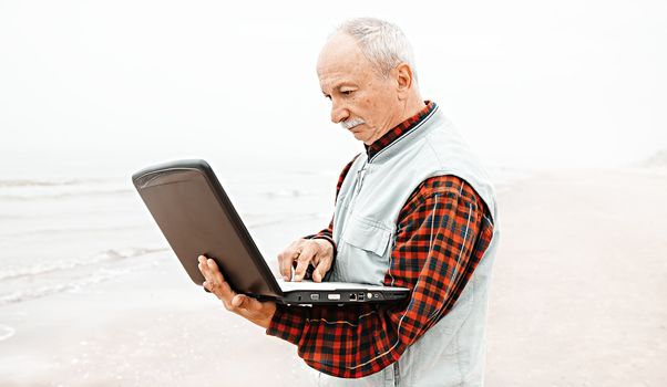 Old man on beach working with notebook on a foggy day