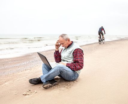 Senior businessman sitting with notebook on the  beach on a foggy day