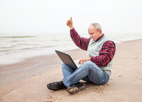 Happy old man sitting with notebook on beach