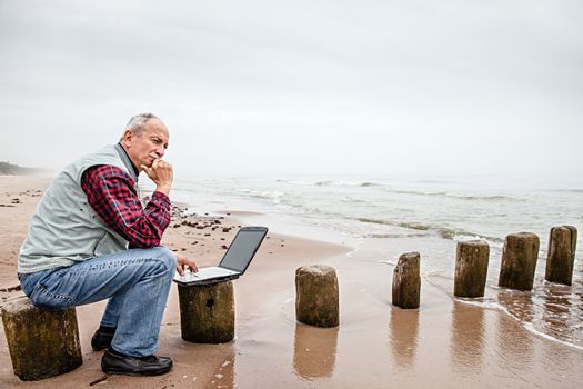 Senior businessman on beach working with notebook