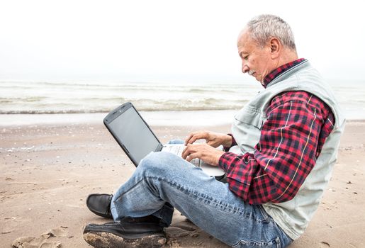 Old man sitting with notebook on sea beach