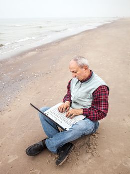 Senior businessman sitting with notebook on beach