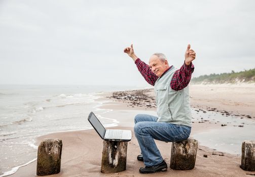 Happy old man with a laptop on the beach on a foggy day