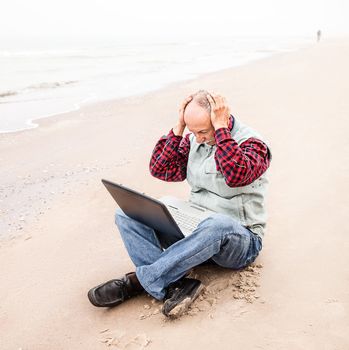 Senior businessman sitting with notebook on beach