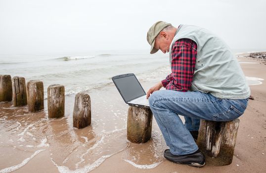 Senior businessman on beach working with notebook