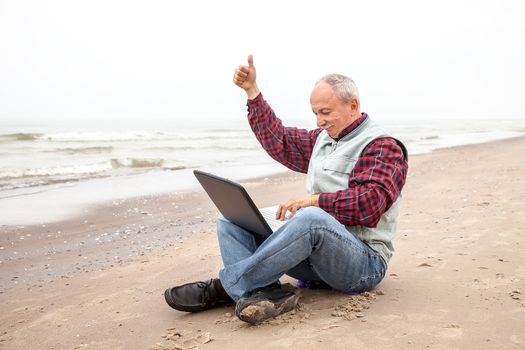 Senior businessman sitting with notebook on beach