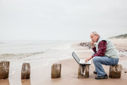 Senior businessman on beach working with notebook on a foggy day