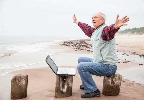 Happy old man with a laptop on the beach on a foggy day