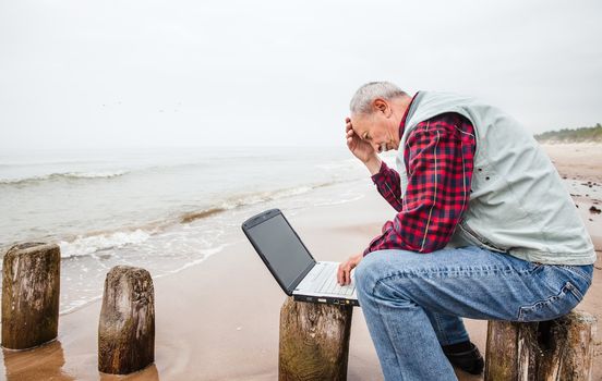 Senior businessman on beach working with notebook