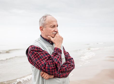 Thoughtful elderly man standing on the beach on a foggy day