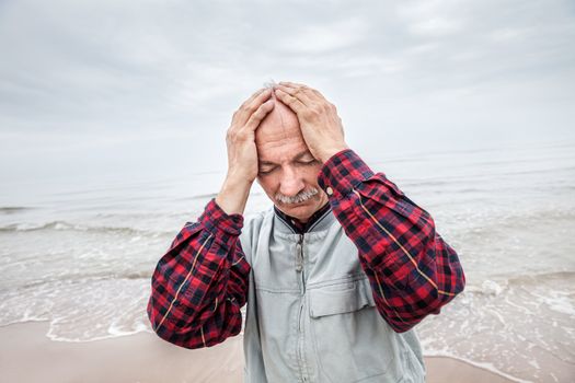 Elderly man suffering from a headache on sea background on foggy day