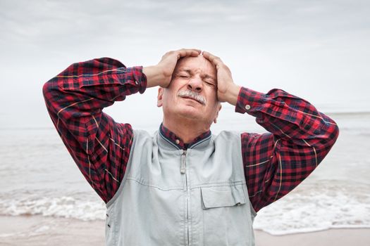 Elderly man suffering from a headache on sea background on foggy day