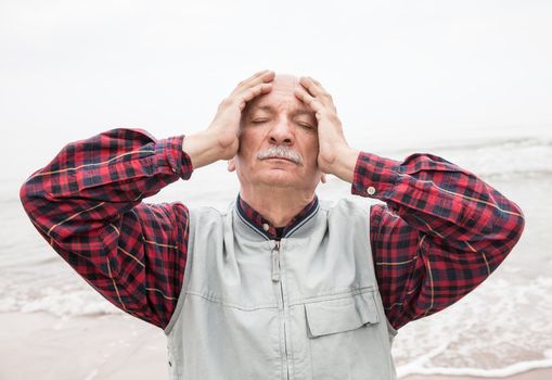 Elderly man suffering from a headache on sea background on foggy day