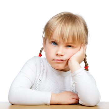 Portrait of unhappy little girl sitting at desk with hand on chin