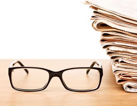 News concept — glasses on a table with stack of newspapers