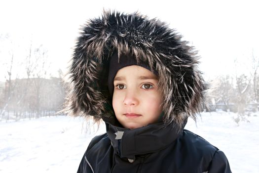 Young boy portrait with furry hood looking at the distance on winter background