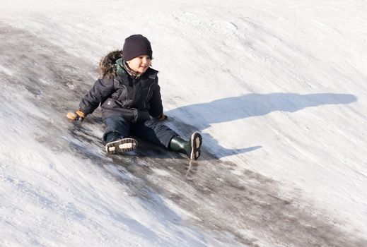 Little boy drive on winter snow hill