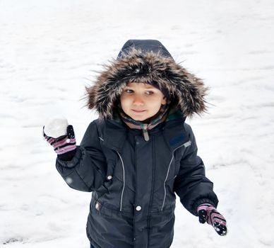 Cute boy in snowsuit holding snowball