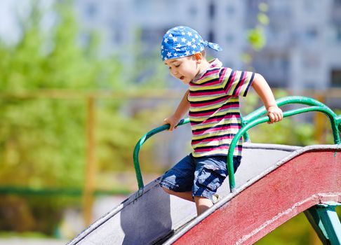 Cute boy in bandana playing on slide