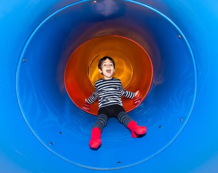 Joyful kid sliding in tube slide on playground