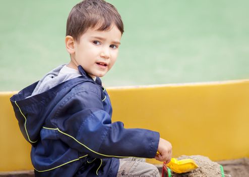 Cute boy in jacket playing in sandbox