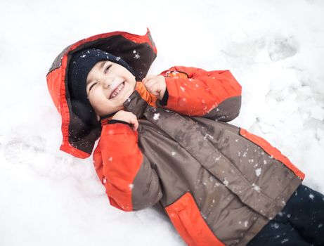 Portrait of little happy boy lies in snow