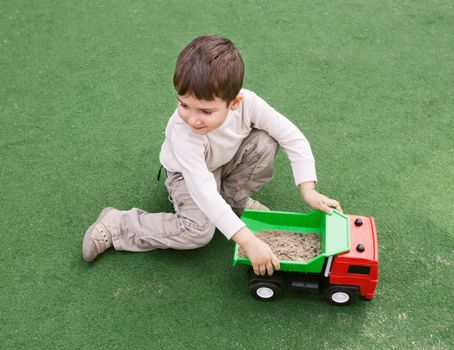 Smiling little boy plays on green grass with toy car