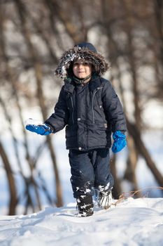 Cute boy in a winter jacket, playing with snow