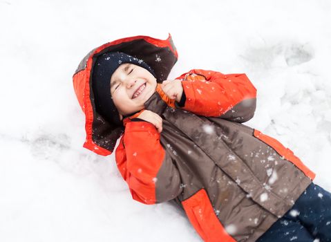 Portrait of little happy boy lies in snow