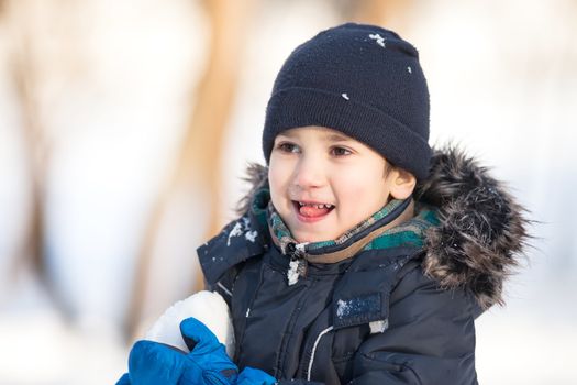 Cute boy in a winter jacket, playing with snow