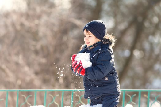 Cute boy in a winter jacket, playing with snow