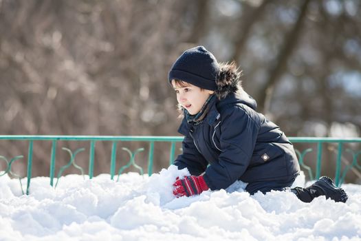 Cute boy in a winter jacket, playing with snow